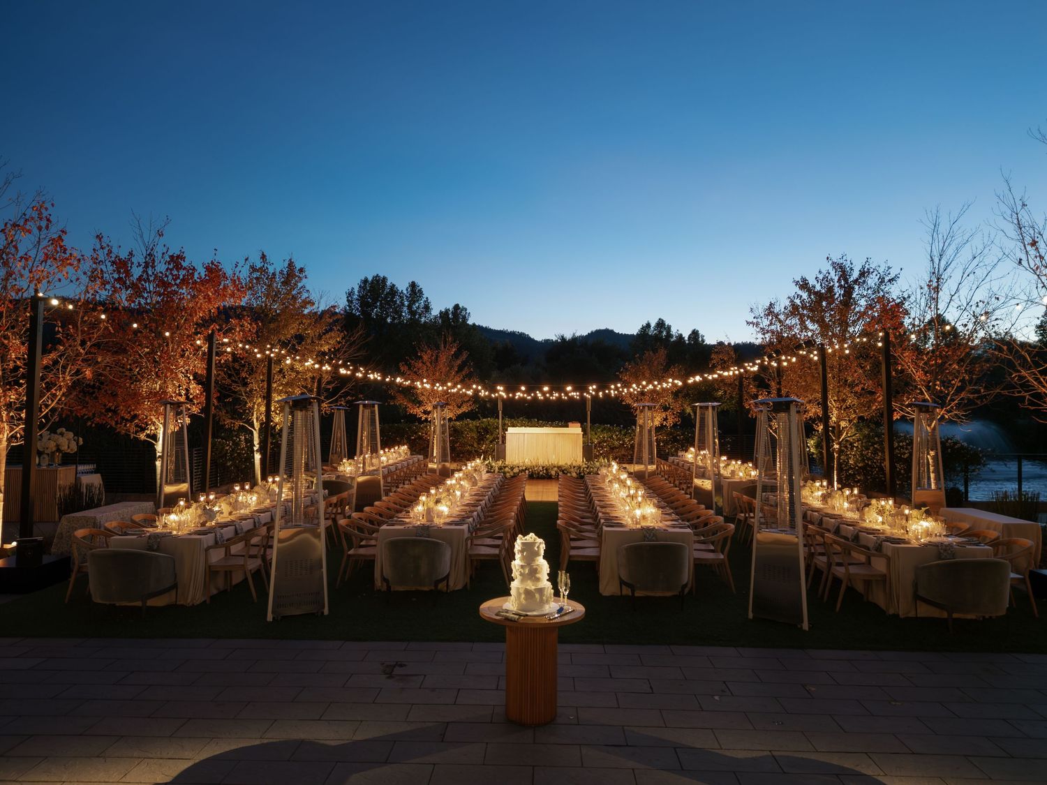 Outdoor wedding reception venue illuminated with string lights at dusk.