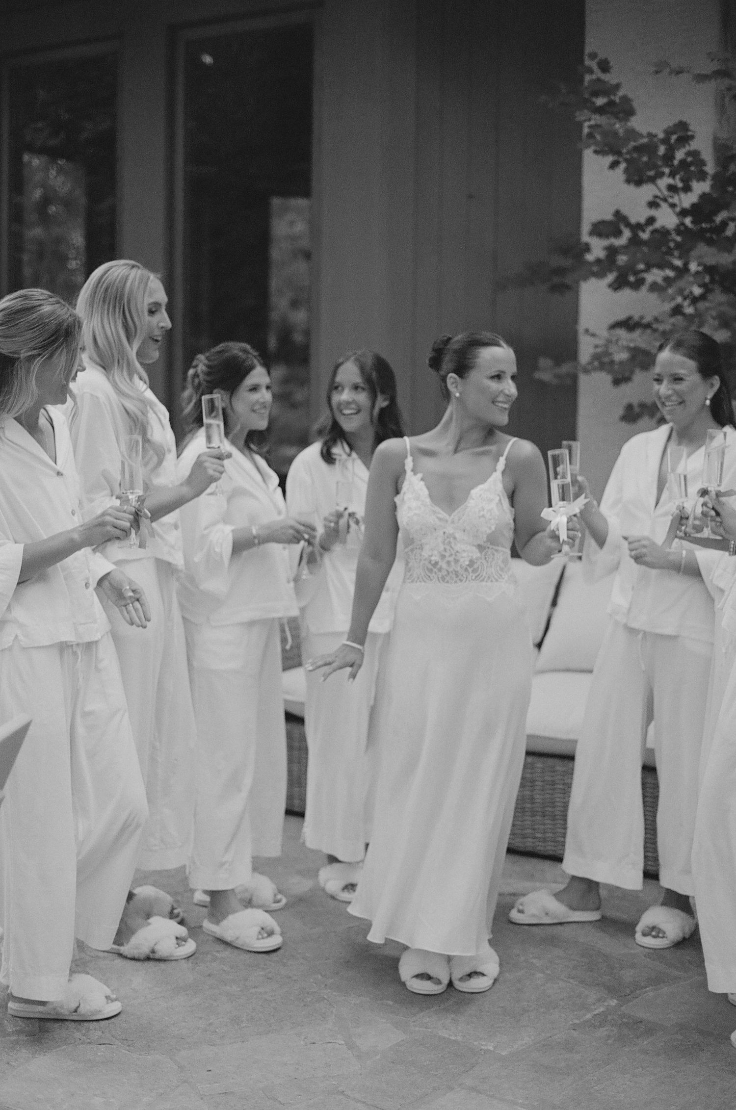 Row of bridesmaids in white robes lined up against a wall during wedding preparations.