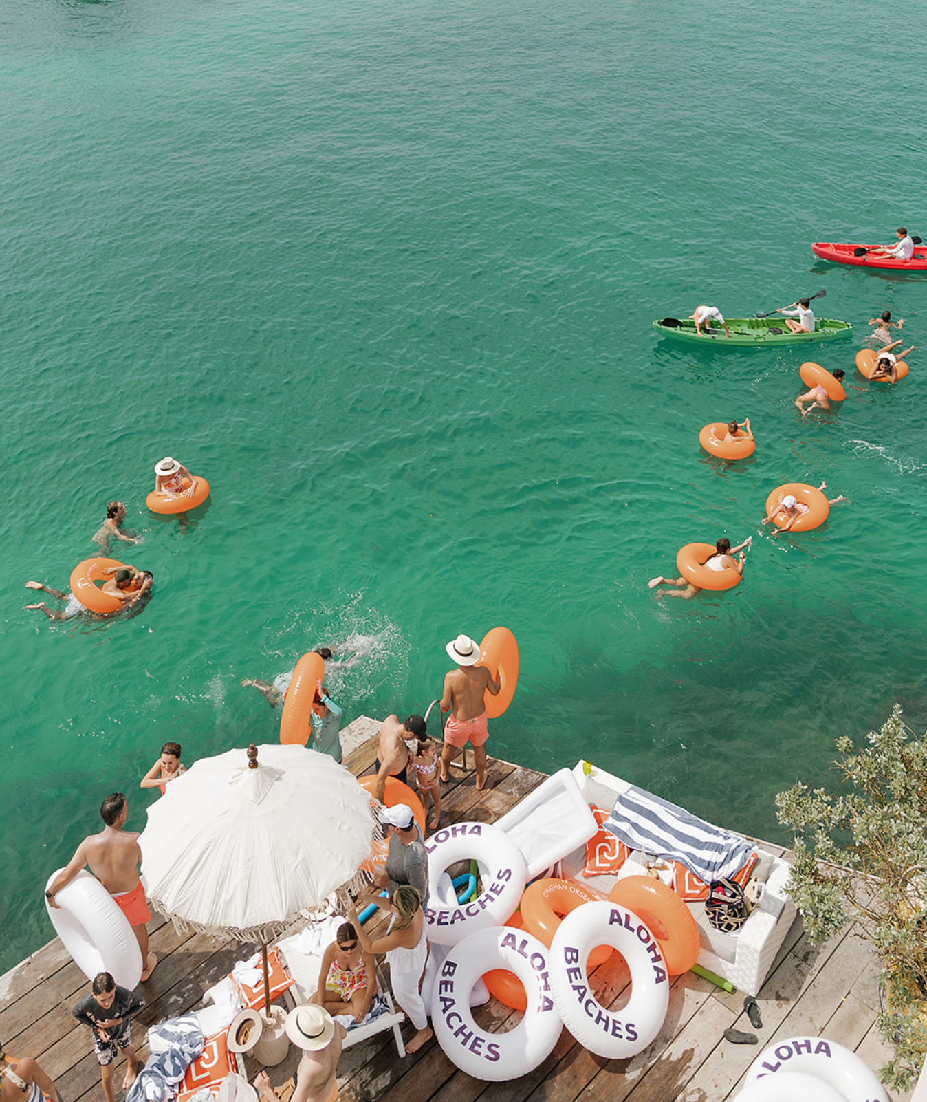 People relaxing on orange floaties in crystal clear turquoise water by a wooden dock.