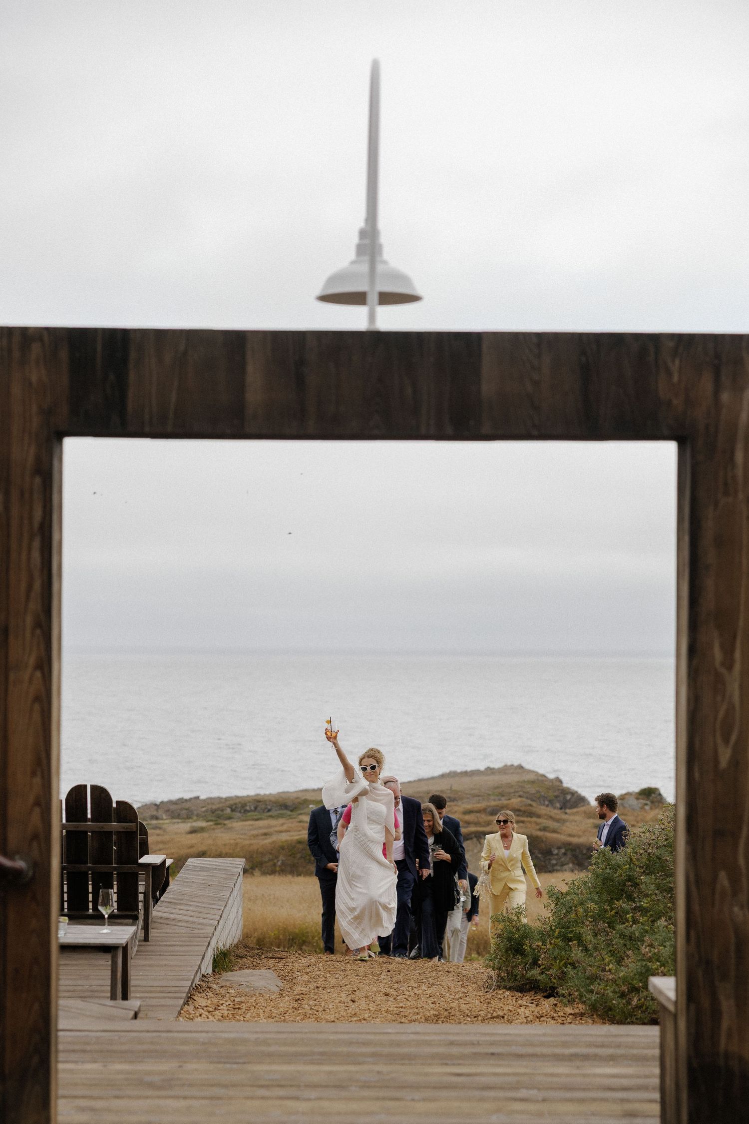Wedding celebration on a coastal deck overlooking the ocean with white tent in background.