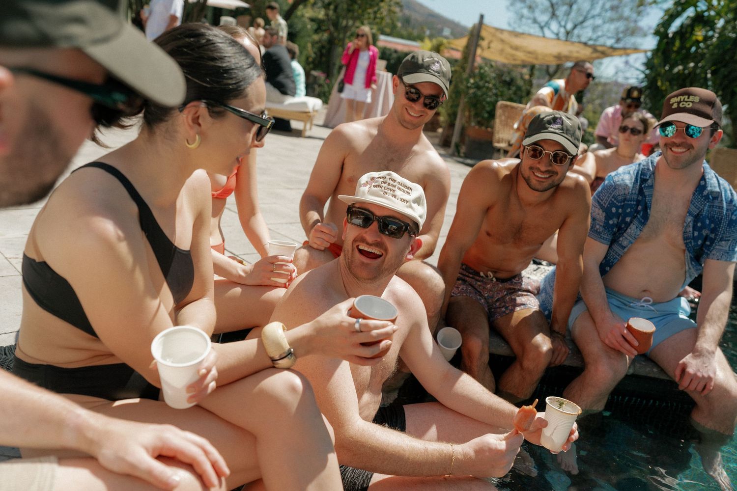 Pool party guests enjoying drinks and conversation in the sunshine.