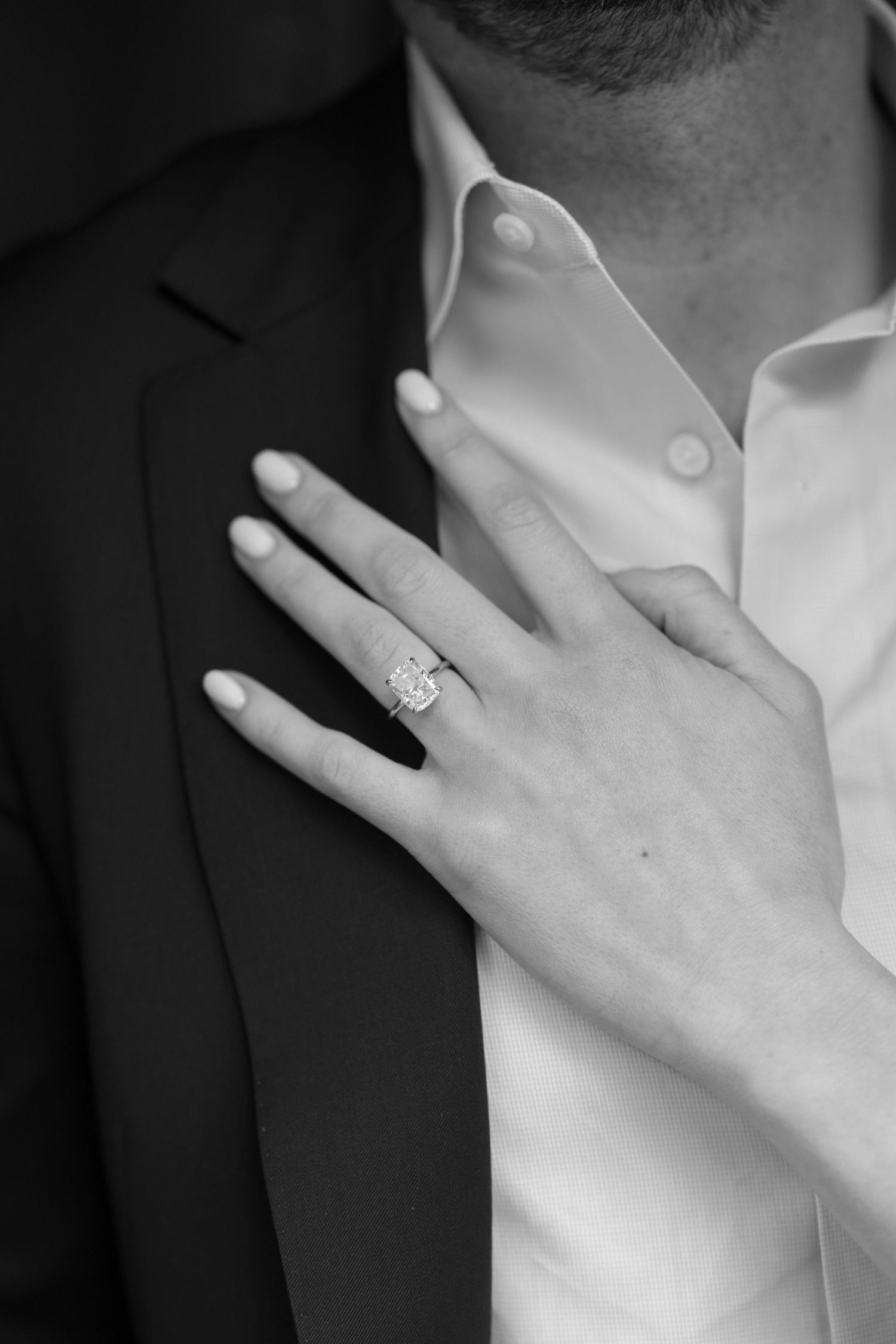 Close-up shot of hands showing an engagement ring against a white and black background.