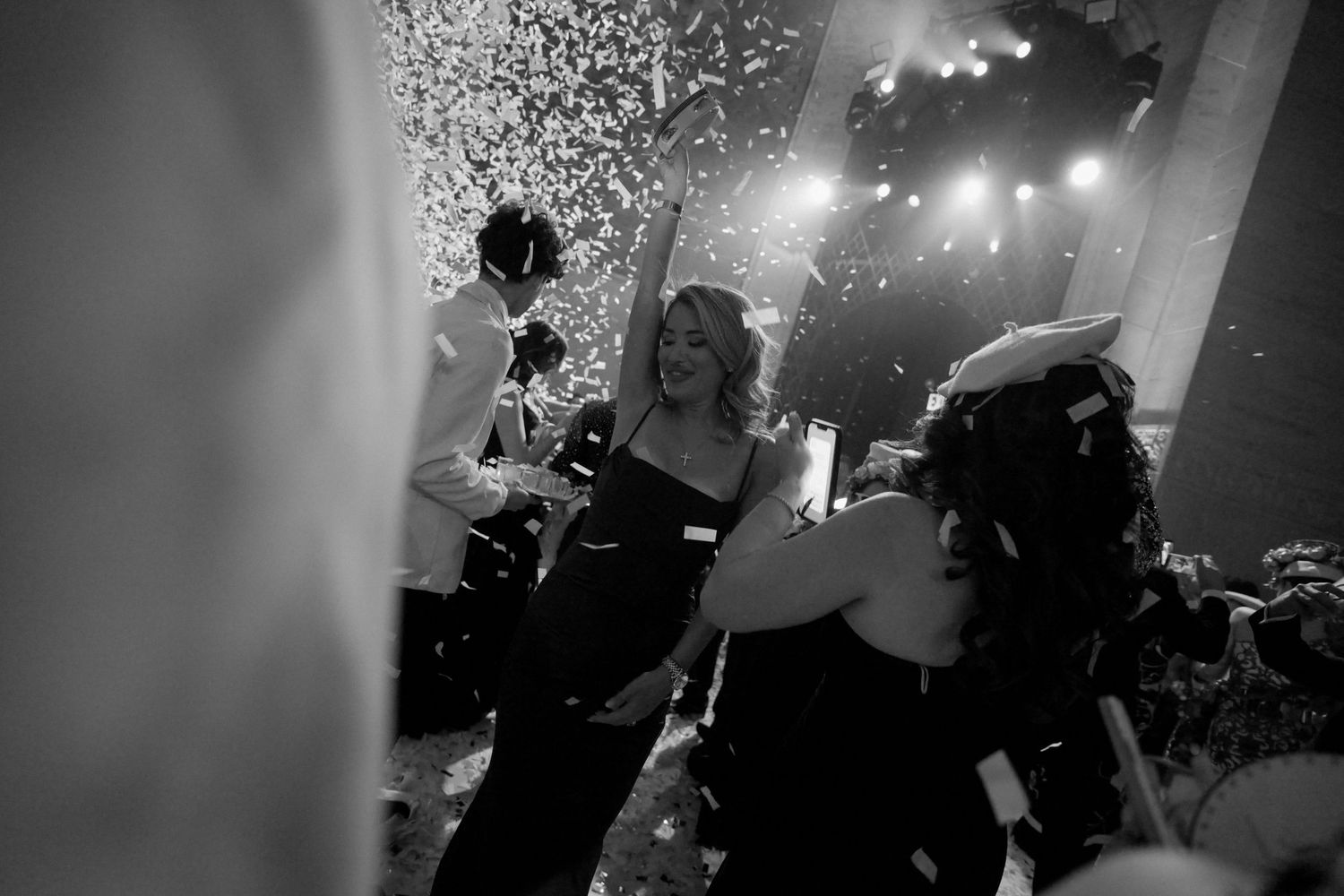 A black and white image of a group of people dancing and celebrating at a festive event.