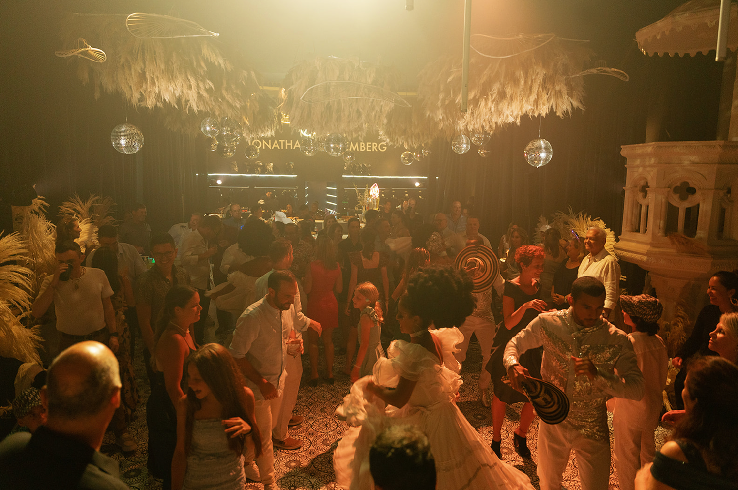 A crowded dance floor bathed in warm golden lighting creates an energetic party atmosphere.