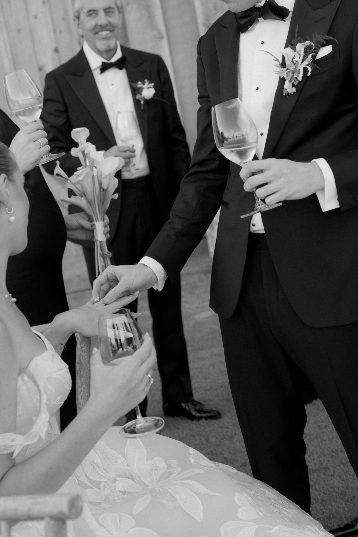 Wedding guests in formal attire share drinks and toasts at outdoor reception.