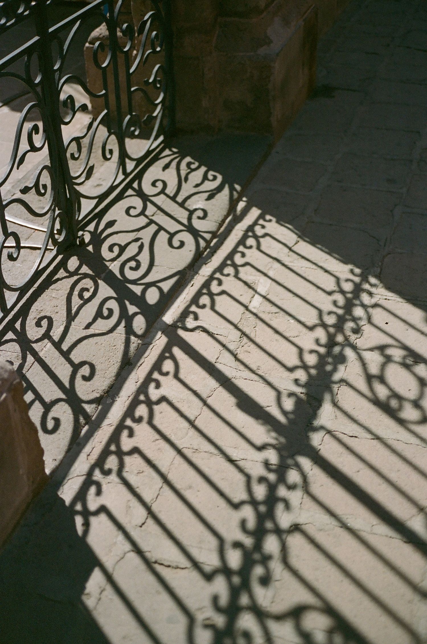 Ornate wrought iron railing casts intricate shadow patterns on a sunlit floor.