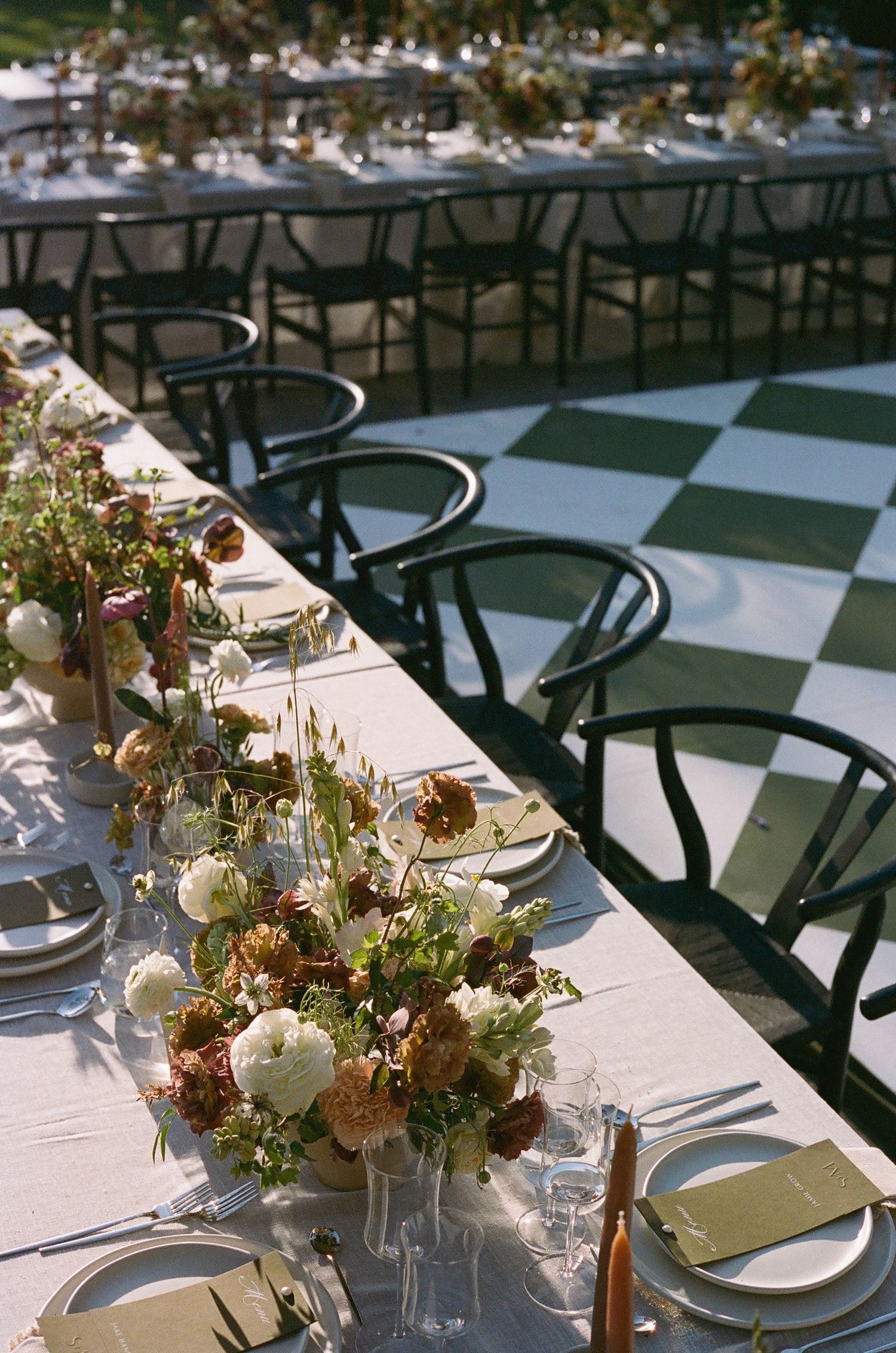 Elegant outdoor wedding reception table setting with floral centerpieces and black chairs.