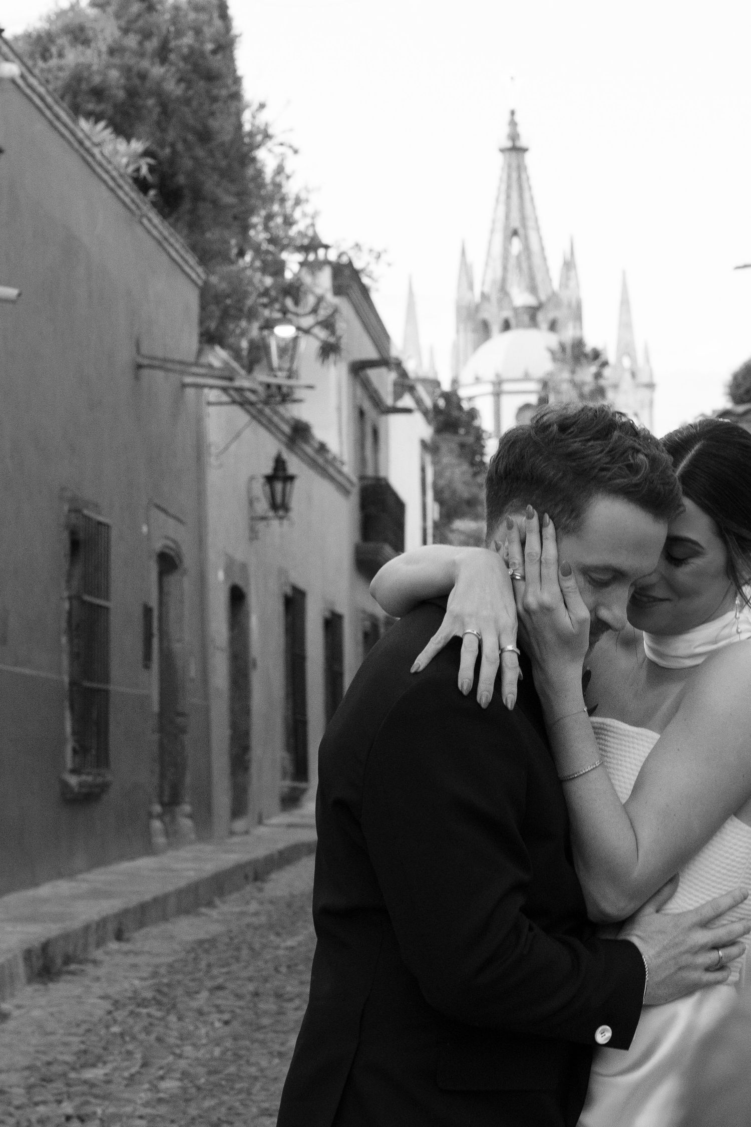 Black and white romantic couple photography series on a cobblestone street with church spires in the background.