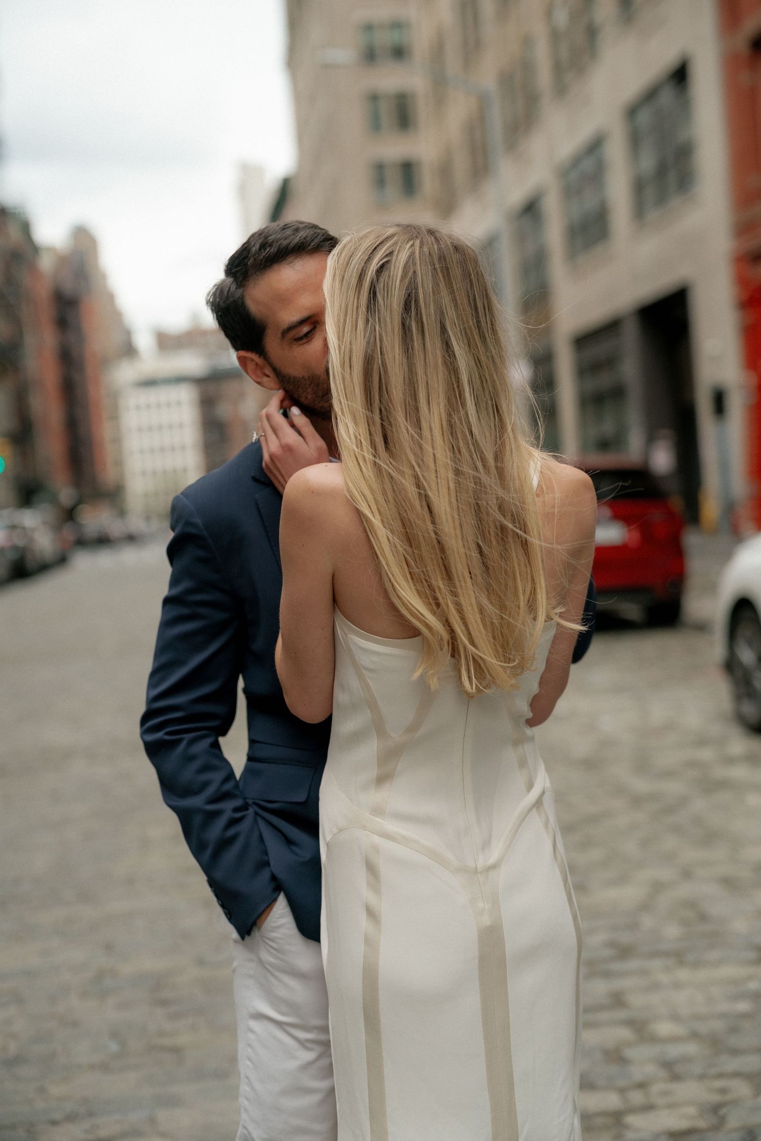 Couple in formal attire sharing an intimate moment on cobblestone street in urban setting.