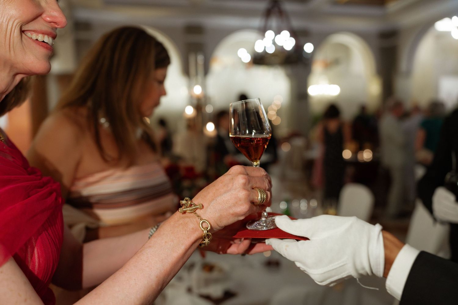 Elegant woman in red dress toasting with wine glass at formal gala dinner event.
