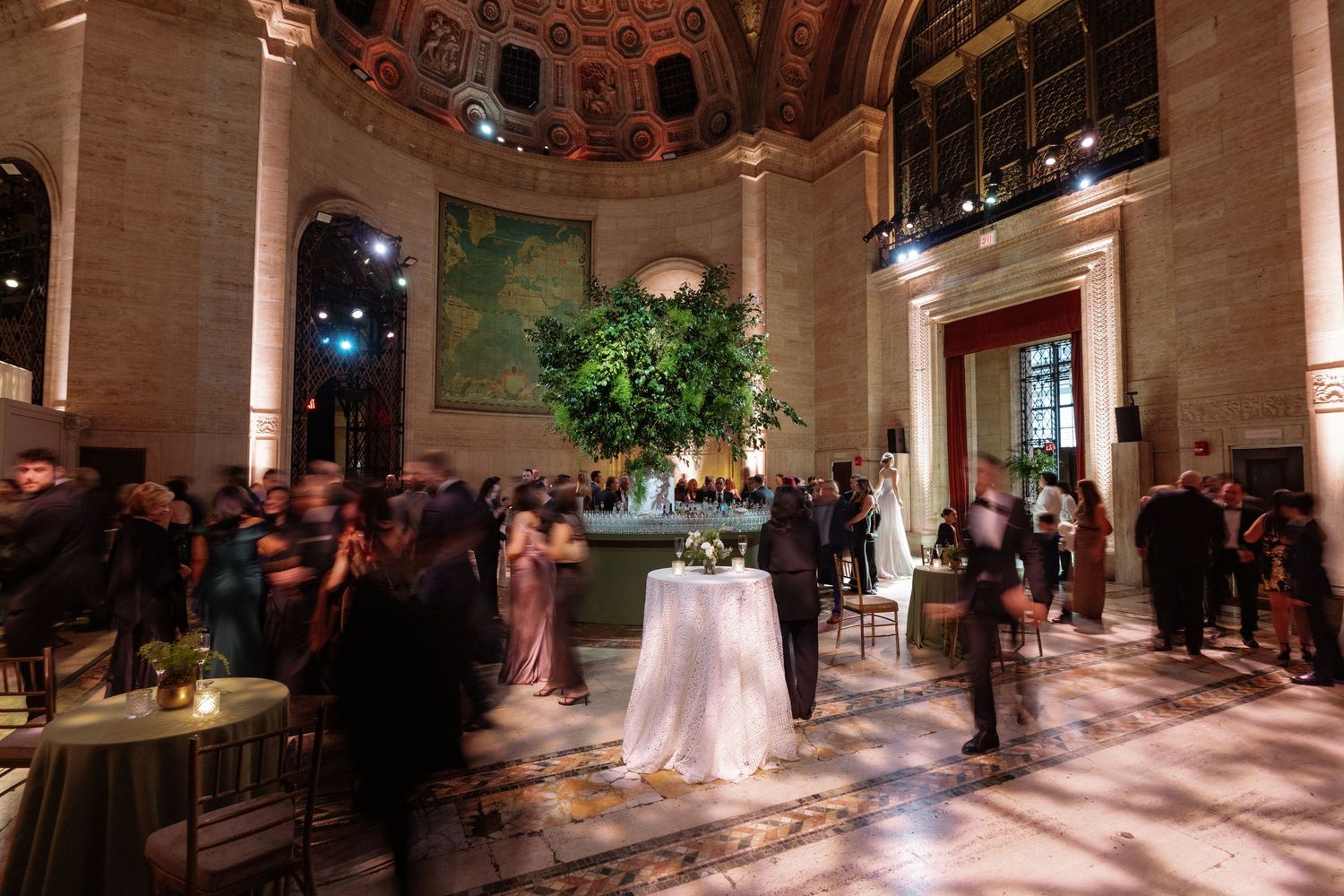 Elegant gala event in a grand hall with ornate ceiling, large floral centerpiece, and guests mingling under warm lights.