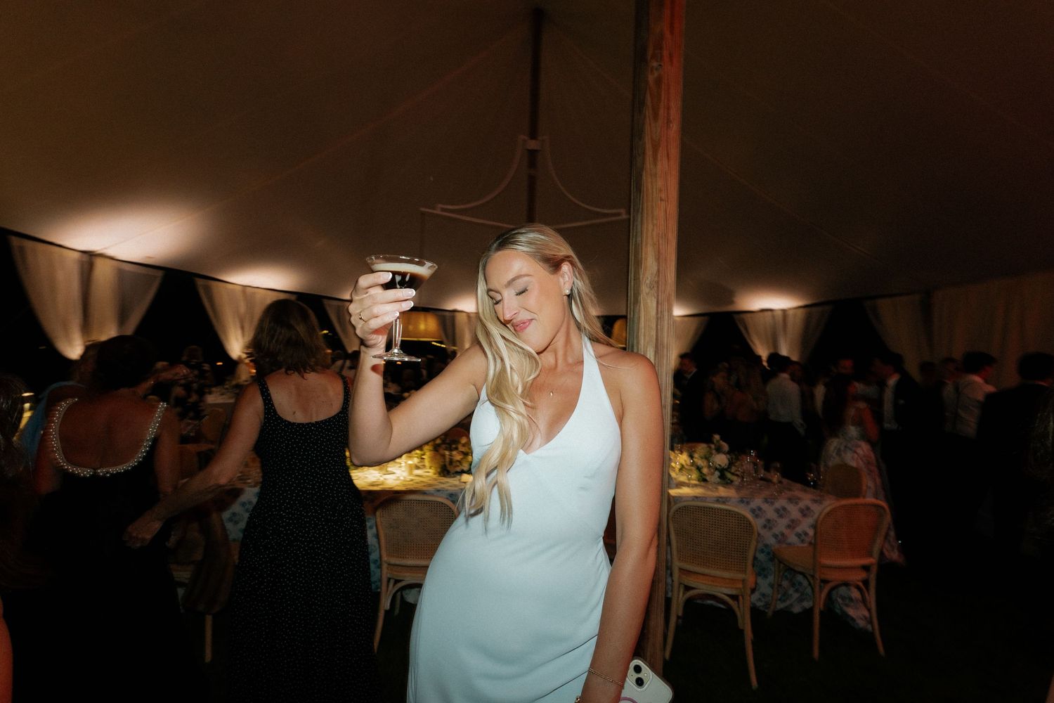 An elegant wedding reception setup inside a tent with ambient lighting and table settings.