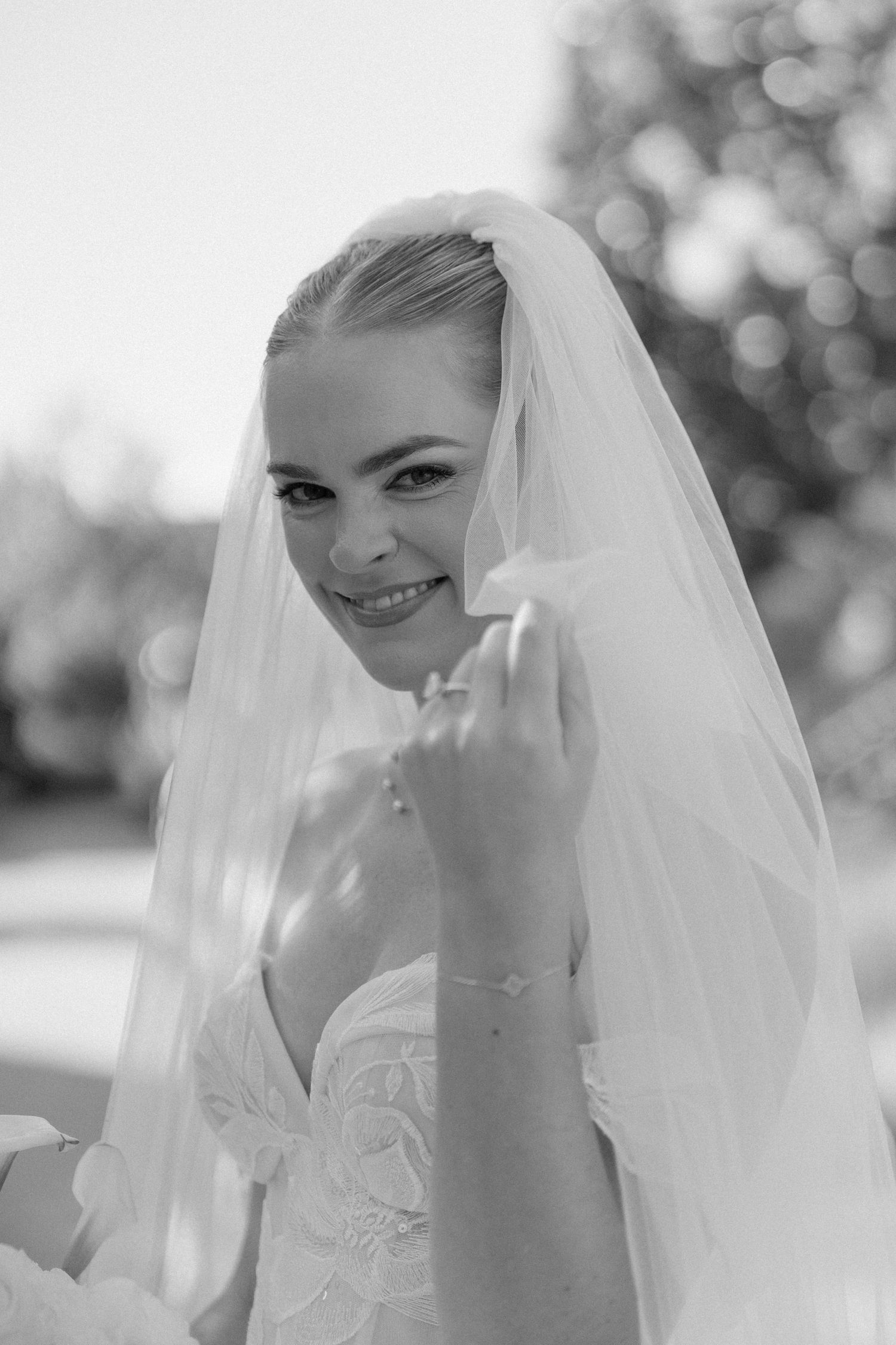 A bride in white dress and veil poses outdoors on her wedding day.