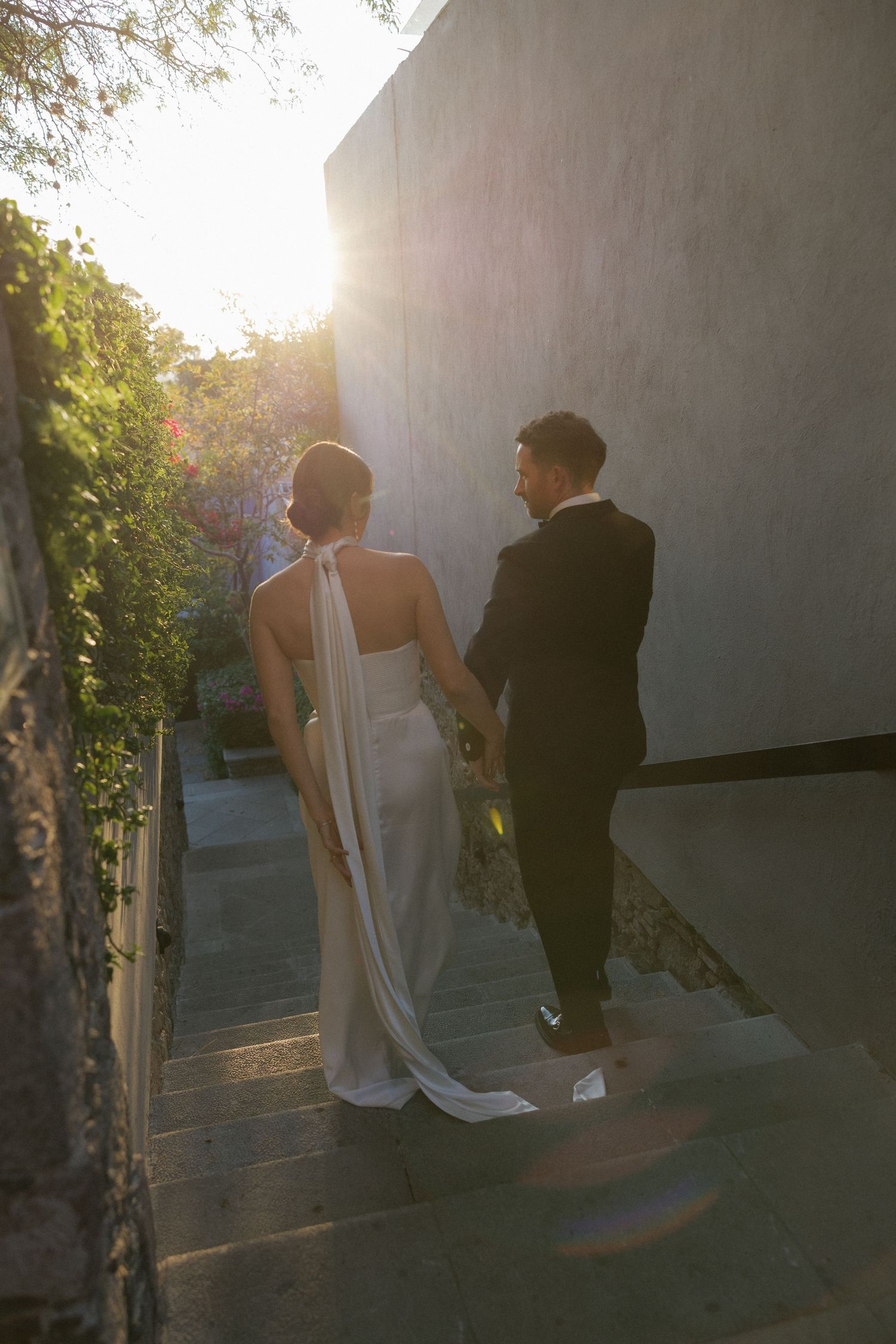 Couple walking up stone steps at sunset in formal attire.