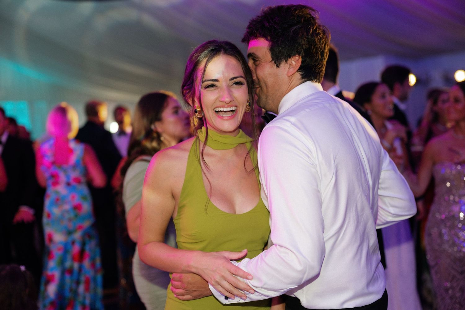 Couples dancing together under colorful party lights at an evening wedding celebration.