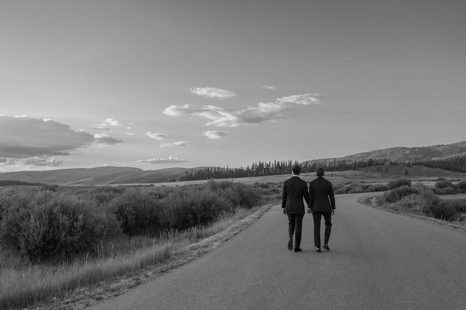 Two silhouettes walking along a scenic mountain road at sunset.