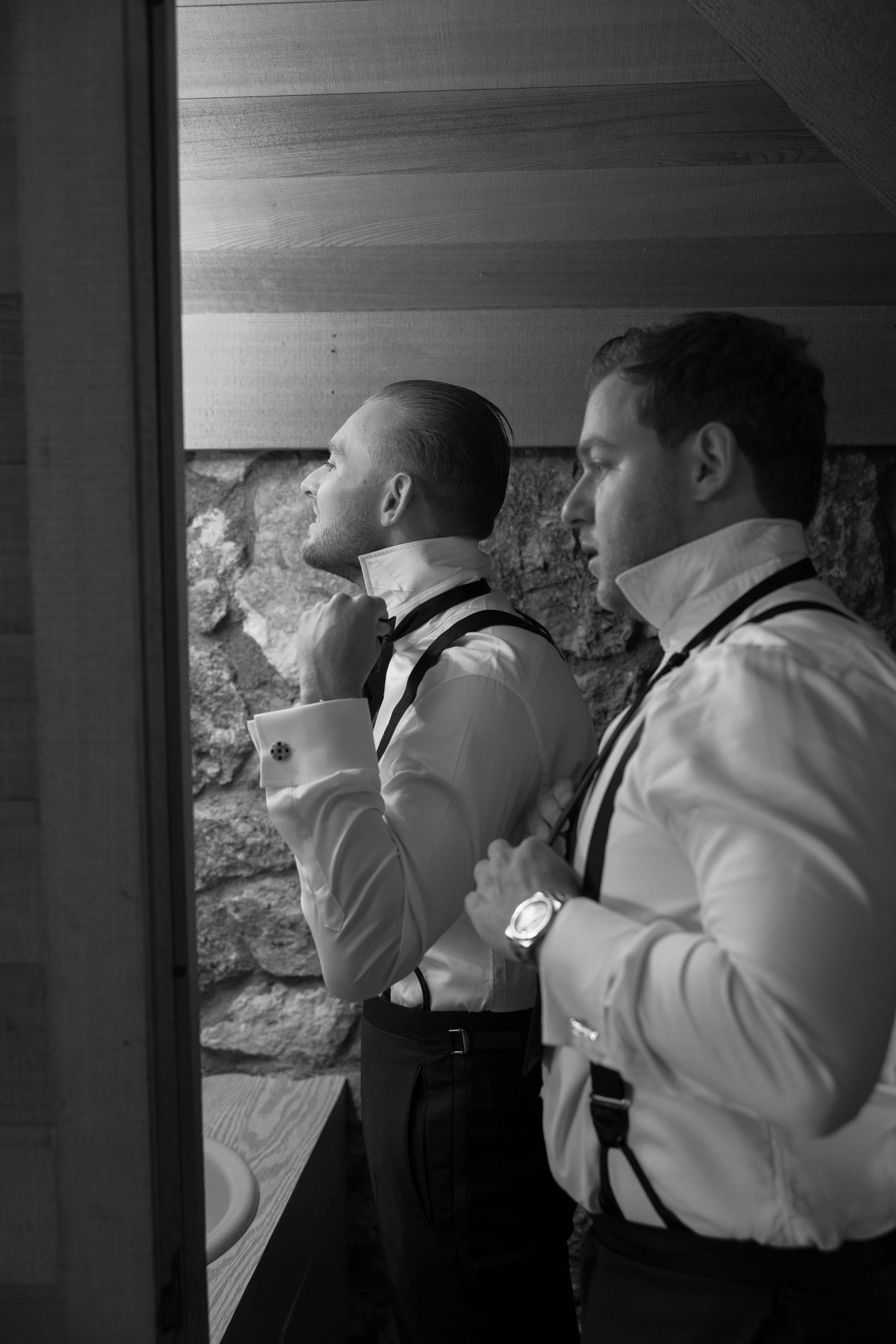 Black and white photo of groomsmen adjusting their ties before a wedding ceremony.