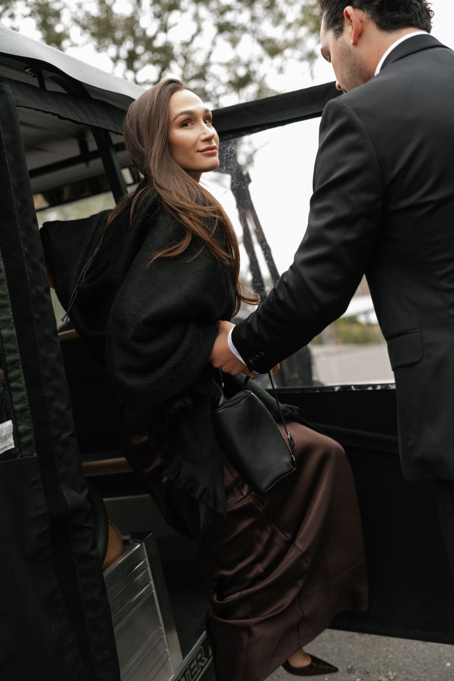 Formal event attendees getting into a black car on an overcast day.
