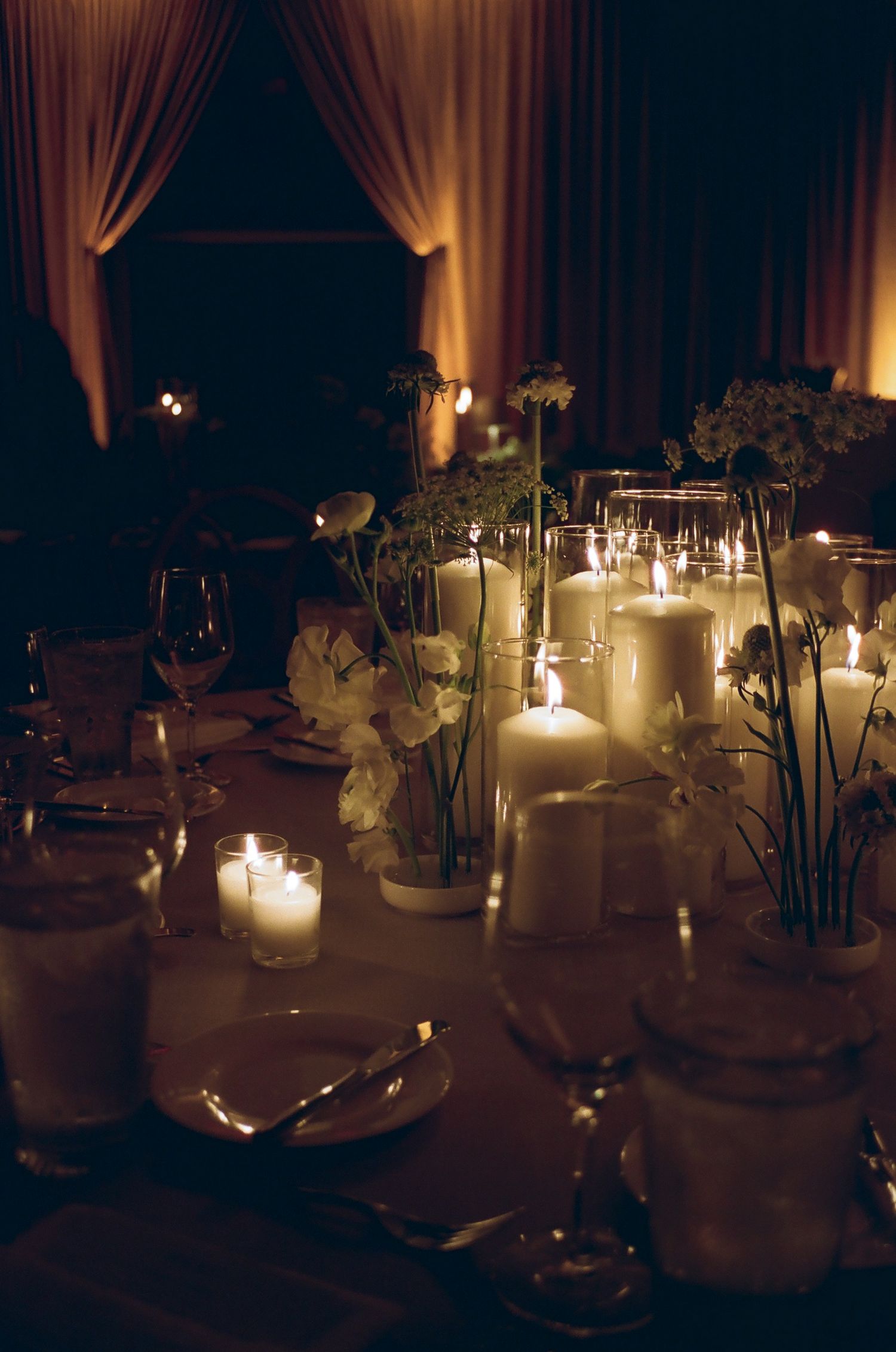 Romantic candlelit wedding reception tables with white floral arrangements.