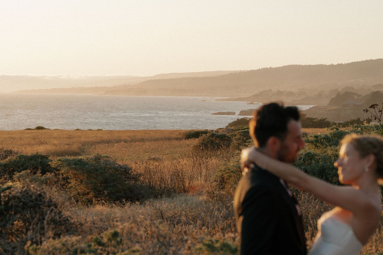 Romantic sunset silhouettes against coastal landscape at outdoor wedding.