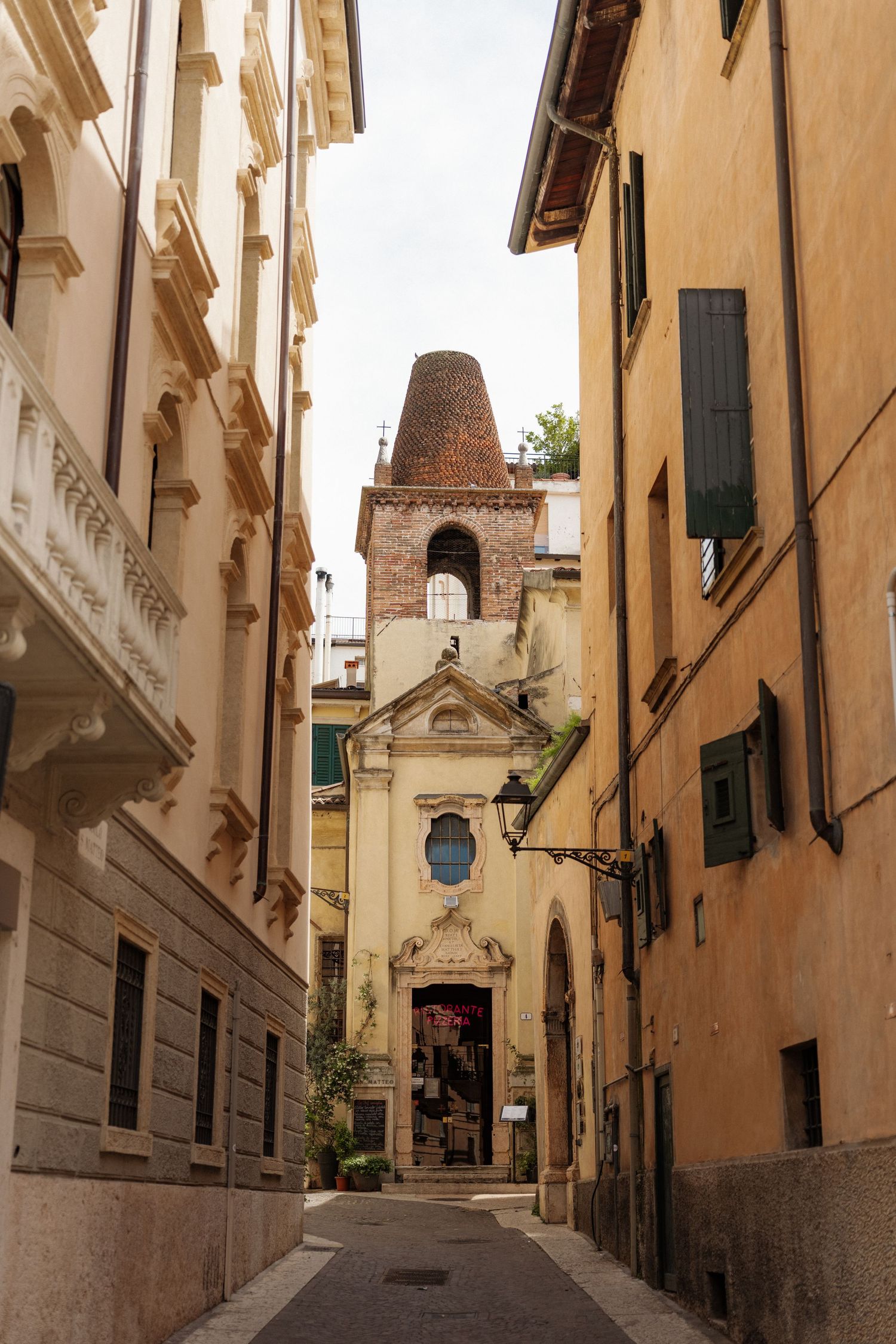Narrow Italian alley leading to a historic church with brick bell tower, flanked by colorful buildings in Verona, Italy.