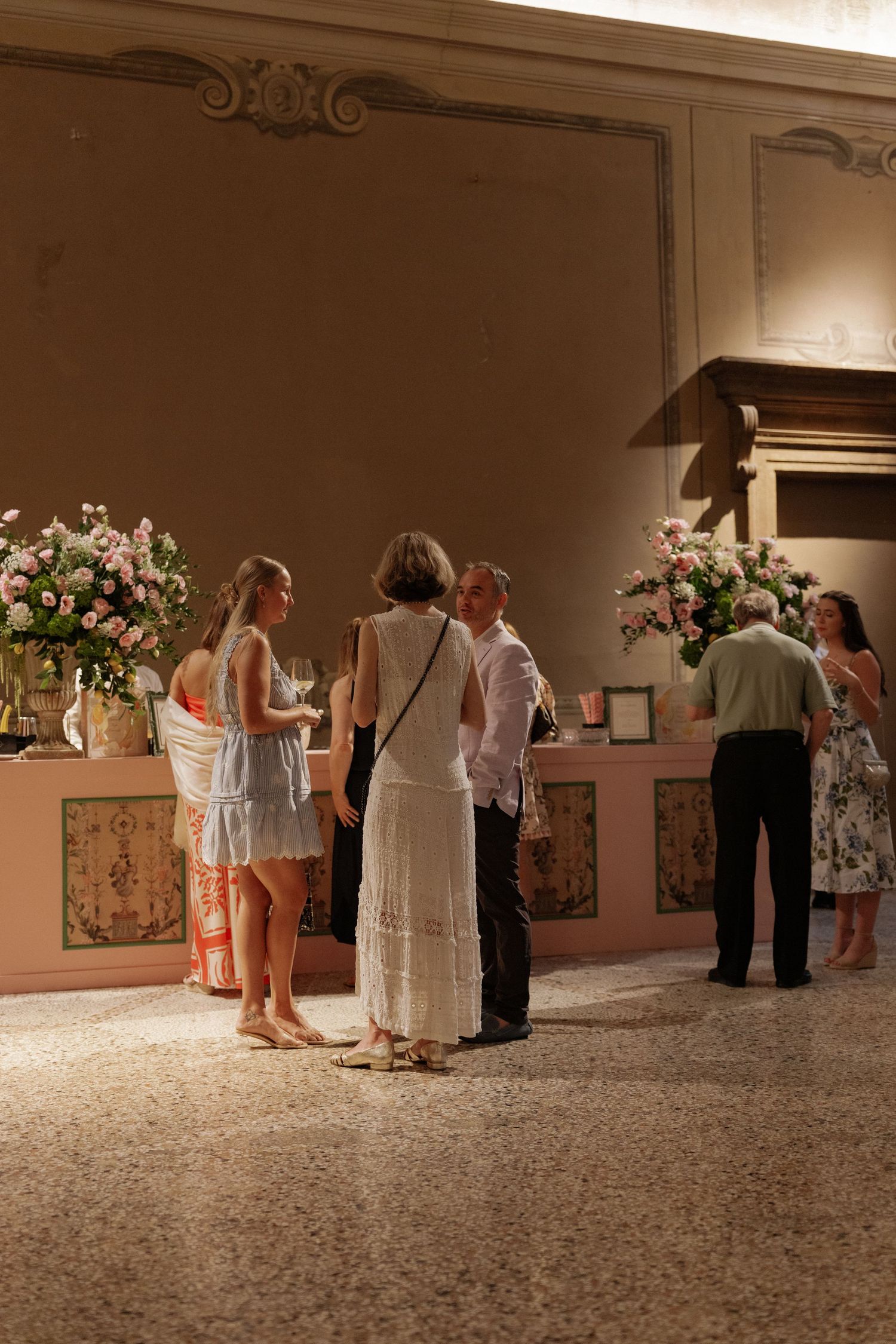 Guests mingling indoors at an elegant event with floral arrangements and warm ambient lighting.