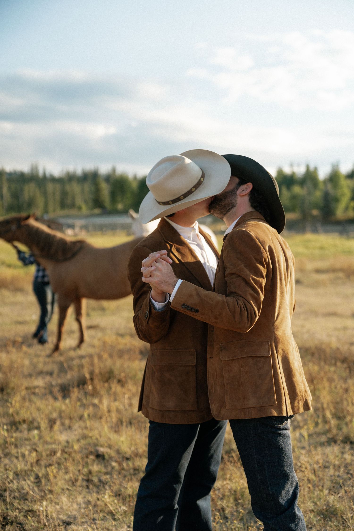 Couple embracing in western attire with horse in background on rustic ranch.