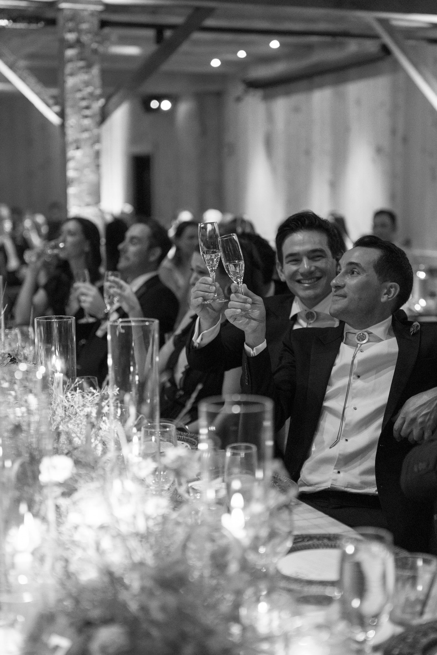 Wedding reception guests raise glasses for a toast among candlelit tables.