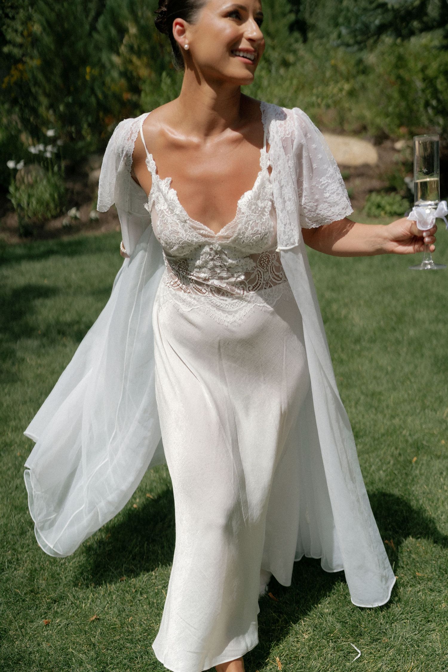 Close-up details of a flowing white wedding dress with lace bodice and sheer sleeves in an outdoor setting.