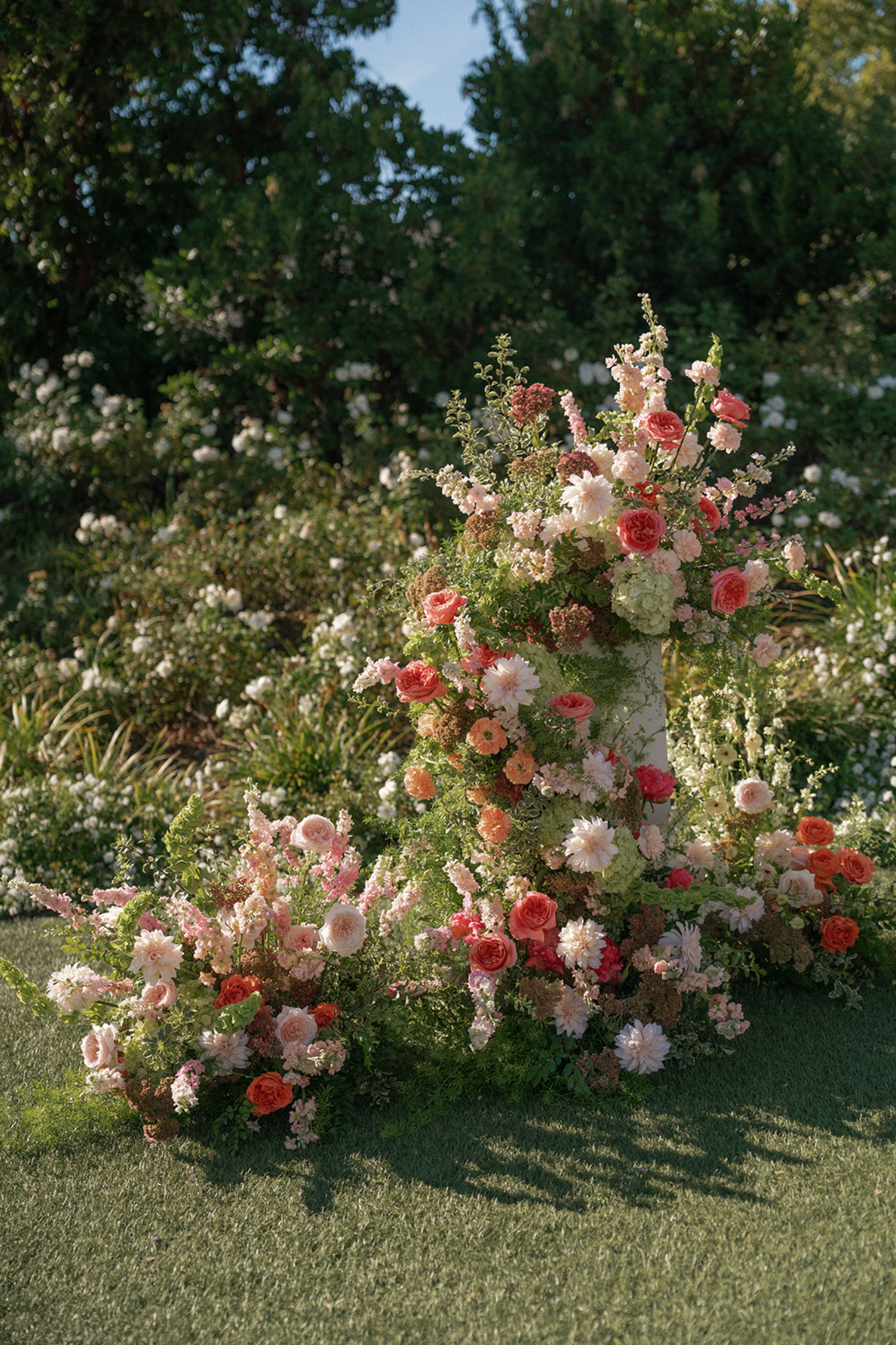 Lush floral arrangement with pink and coral roses cascading on a garden lawn.