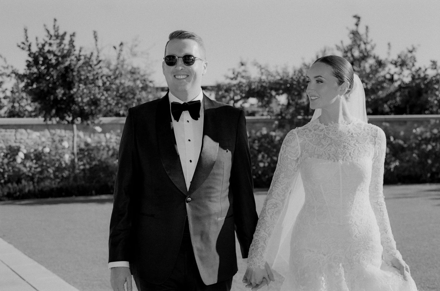 A couple walks together outdoors in formal black and white wedding attire.