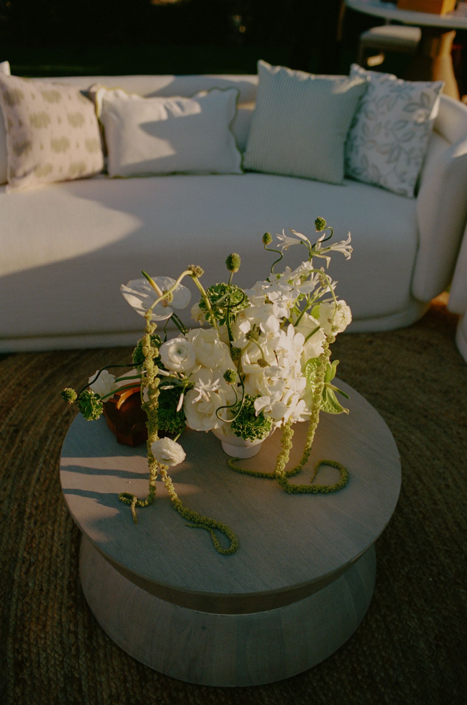 White floral arrangement on round coffee table with modern grey couch.