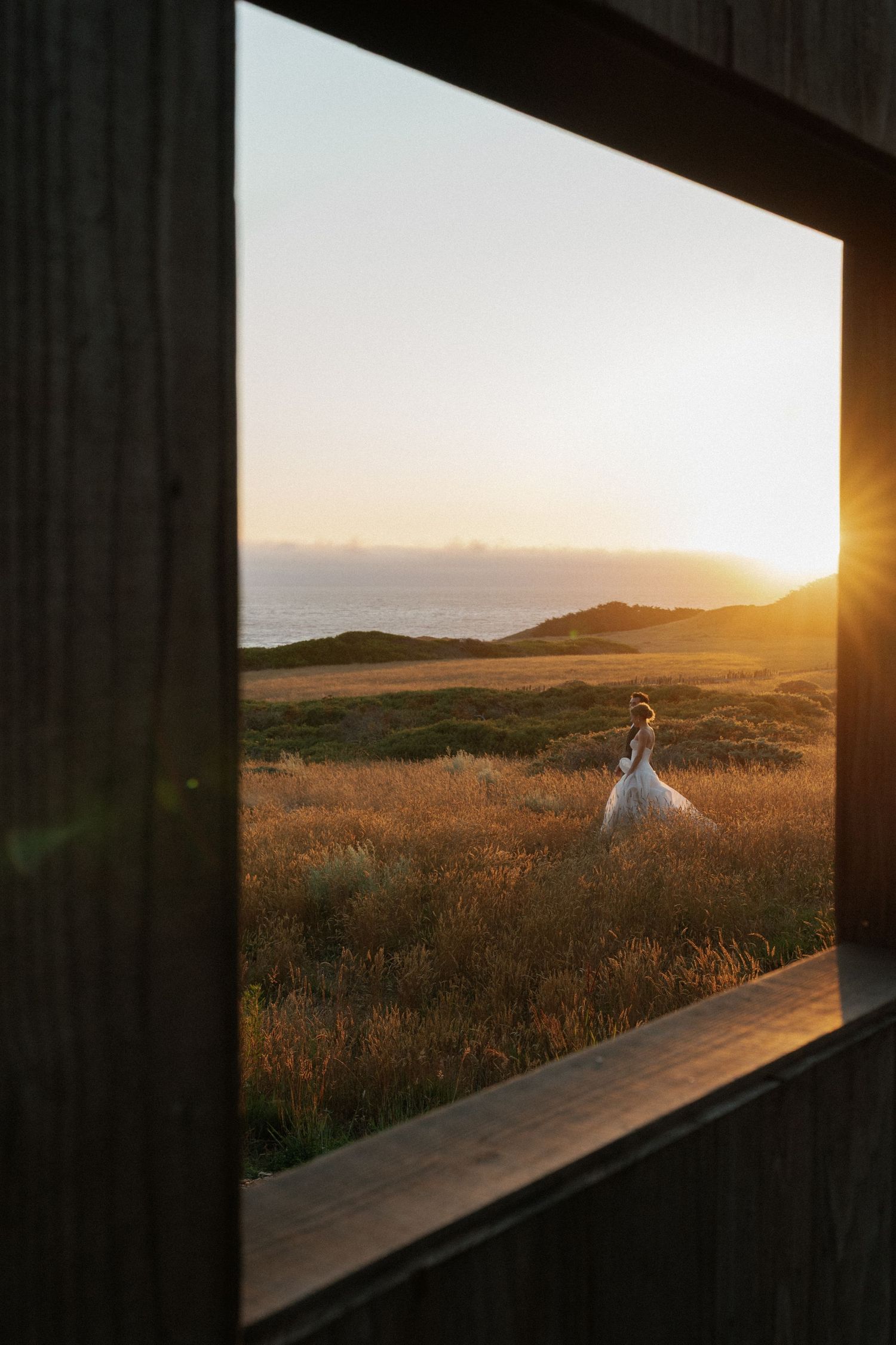 Scenic sunset wedding photos through wooden frame with golden light on rolling hills.