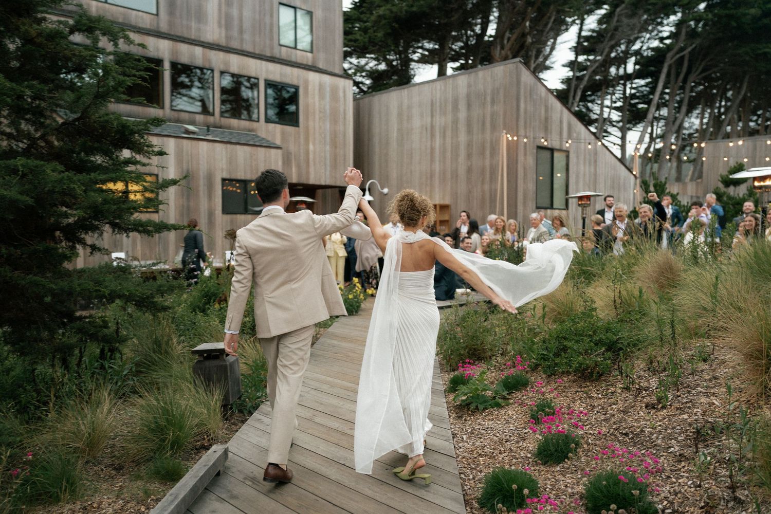 Wedding party walking through a garden path with blooming flowers.