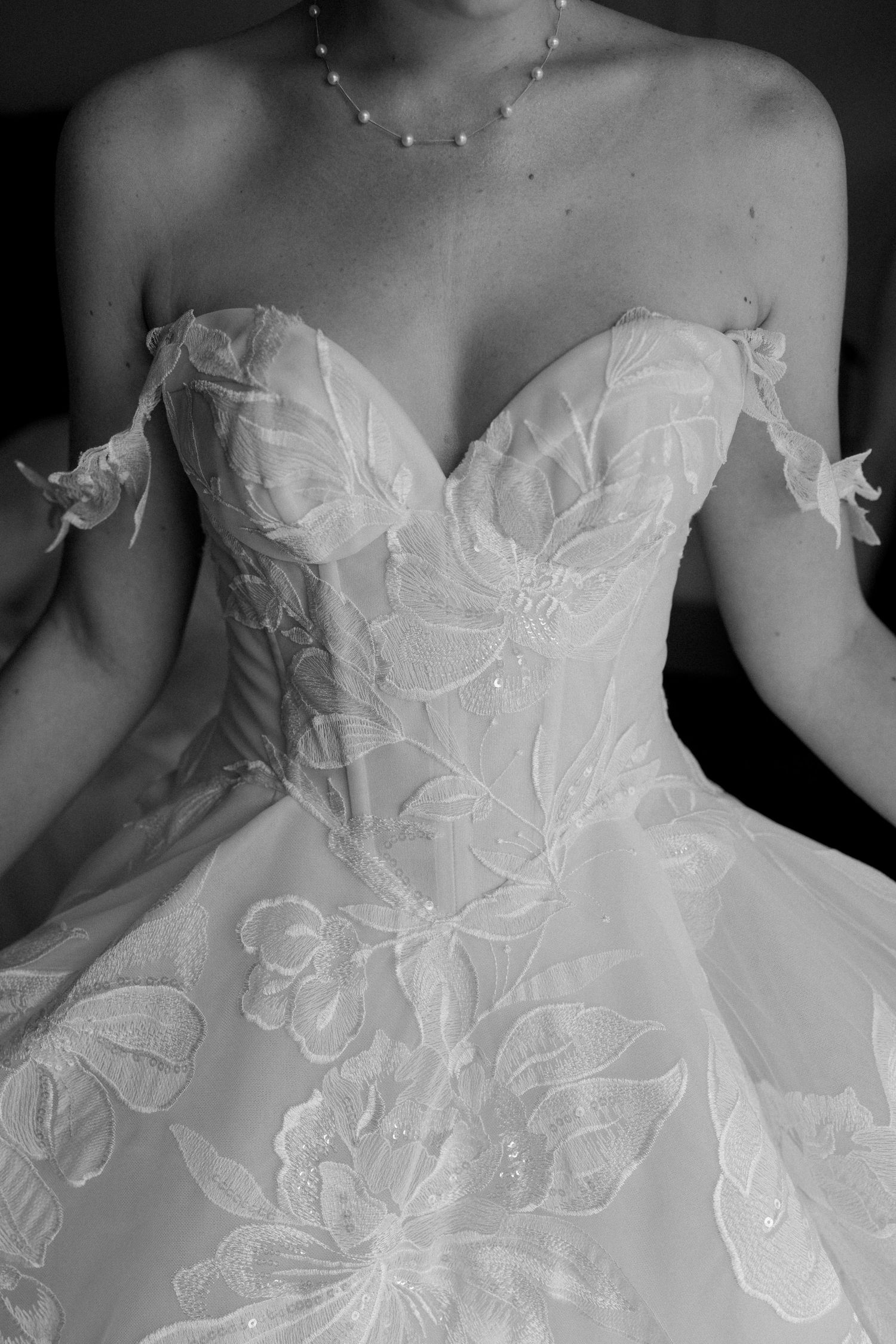 Close-up details of a white wedding dress bodice featuring intricate floral lace appliques and strapless design.