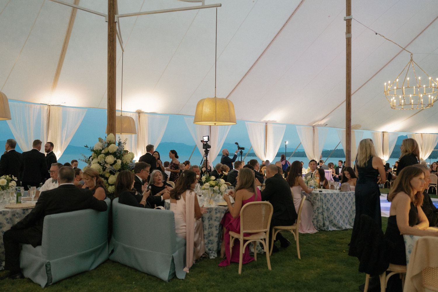 A large outdoor wedding reception tent setup with tables and chairs on a grassy field.