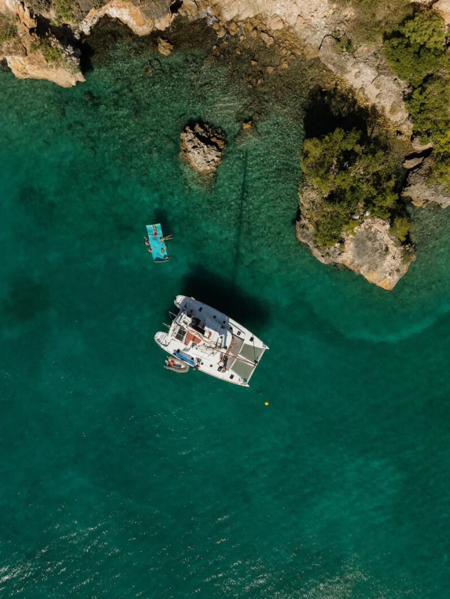 Aerial view of boats anchored in turquoise waters near rocky coastal cliffs.
