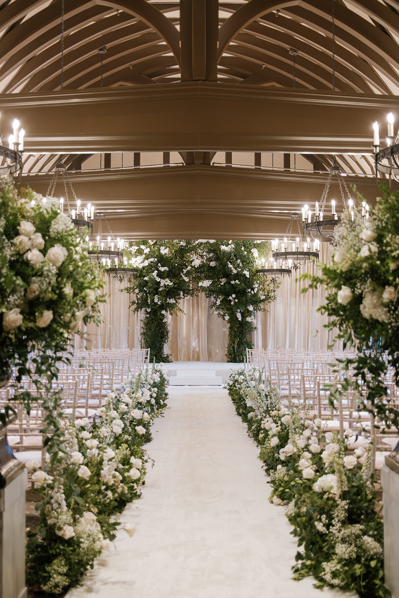 Elegant wedding ceremony space with arched ceiling and white floral arrangements lining the aisle.