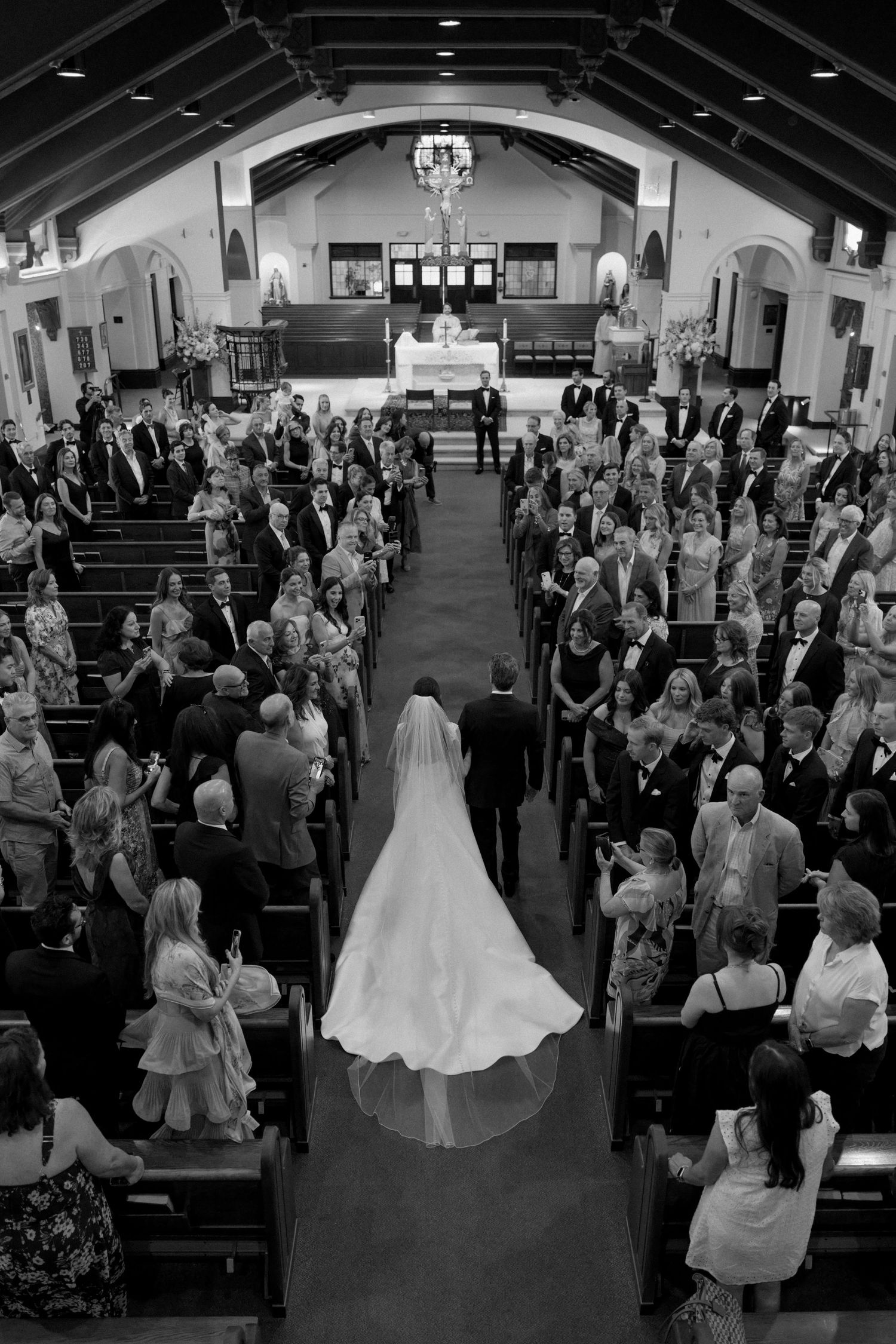 Aerial black and white view of bride walking down church aisle.