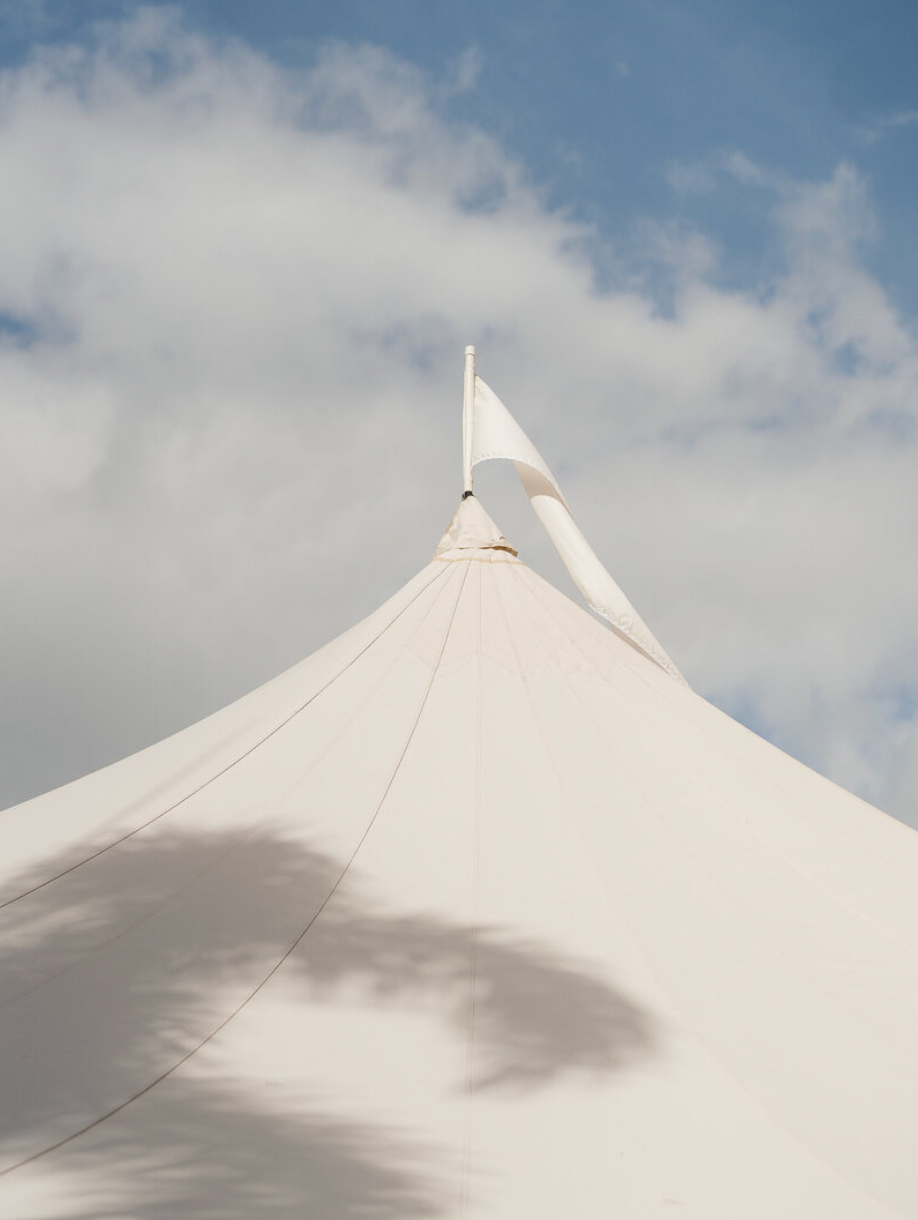 White wedding tent peaks against a blue cloudy sky creating a minimalist architectural view.