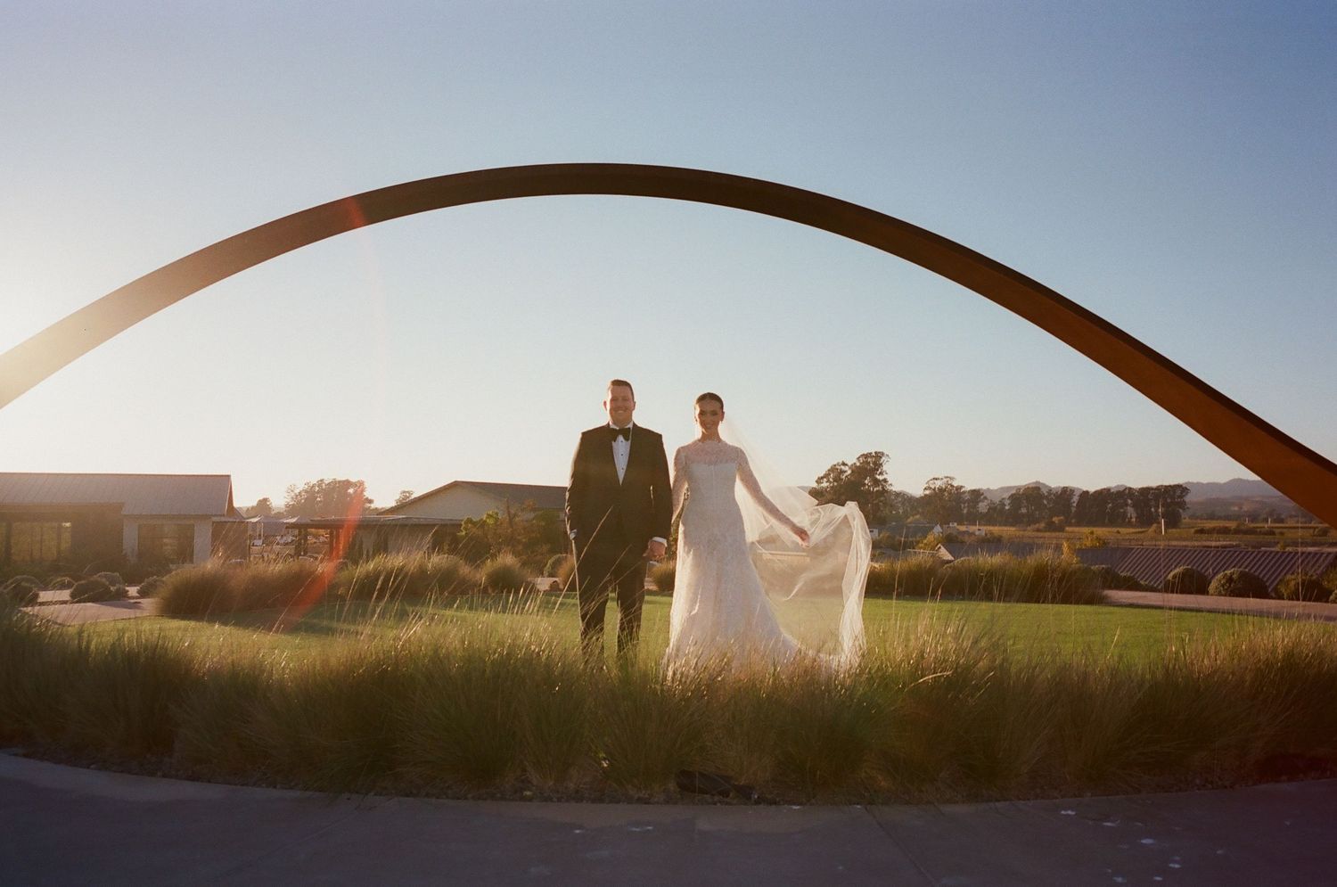 Silhouetted couple under large architectural arch during golden hour.