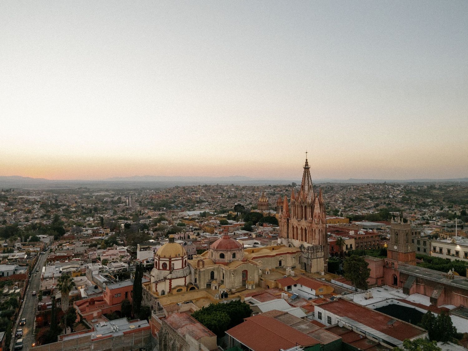 Aerial view of San Miguel de Allende's iconic pink church and cityscape at sunset.