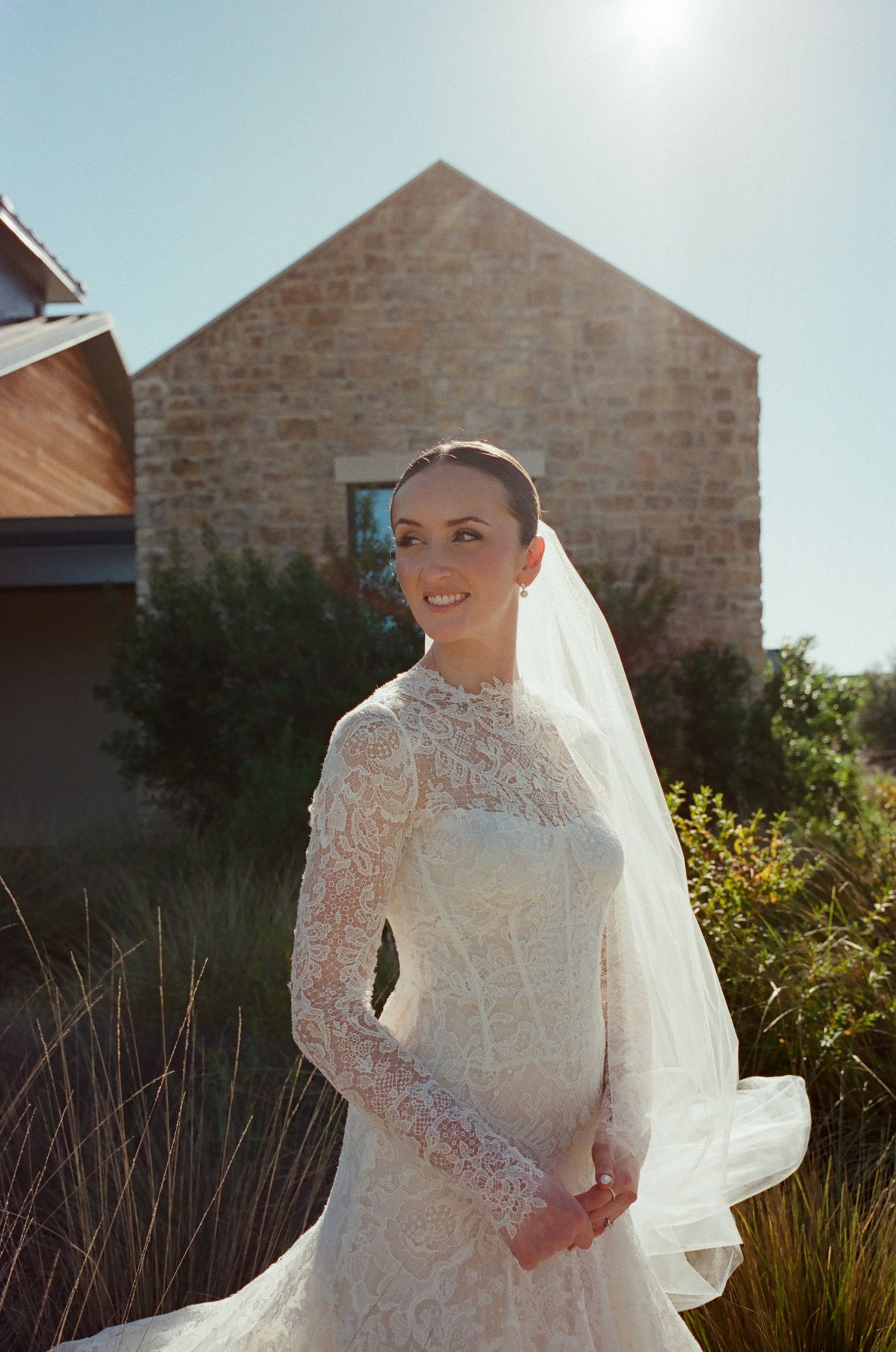 Elegant long-sleeved lace wedding dress with high neckline photographed against stone building.