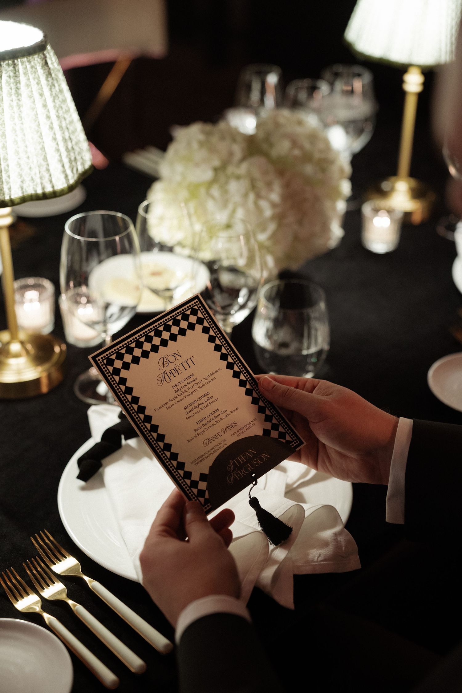 Wedding menu being held at an elegantly set dinner table with candlelight and white floral centerpieces.