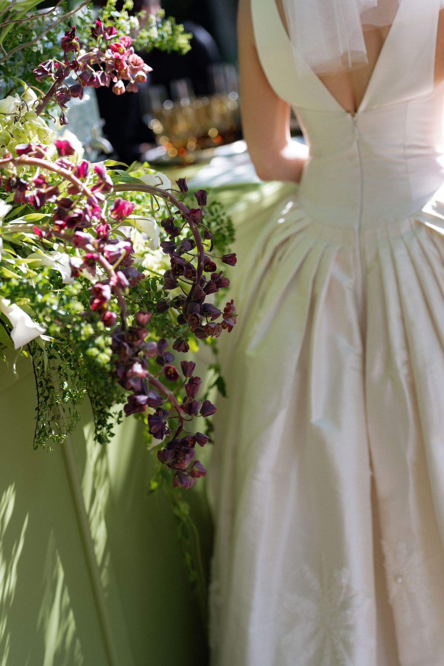 Bride in elegant ivory ball gown standing beside a floral arrangement with cascading purple blooms.