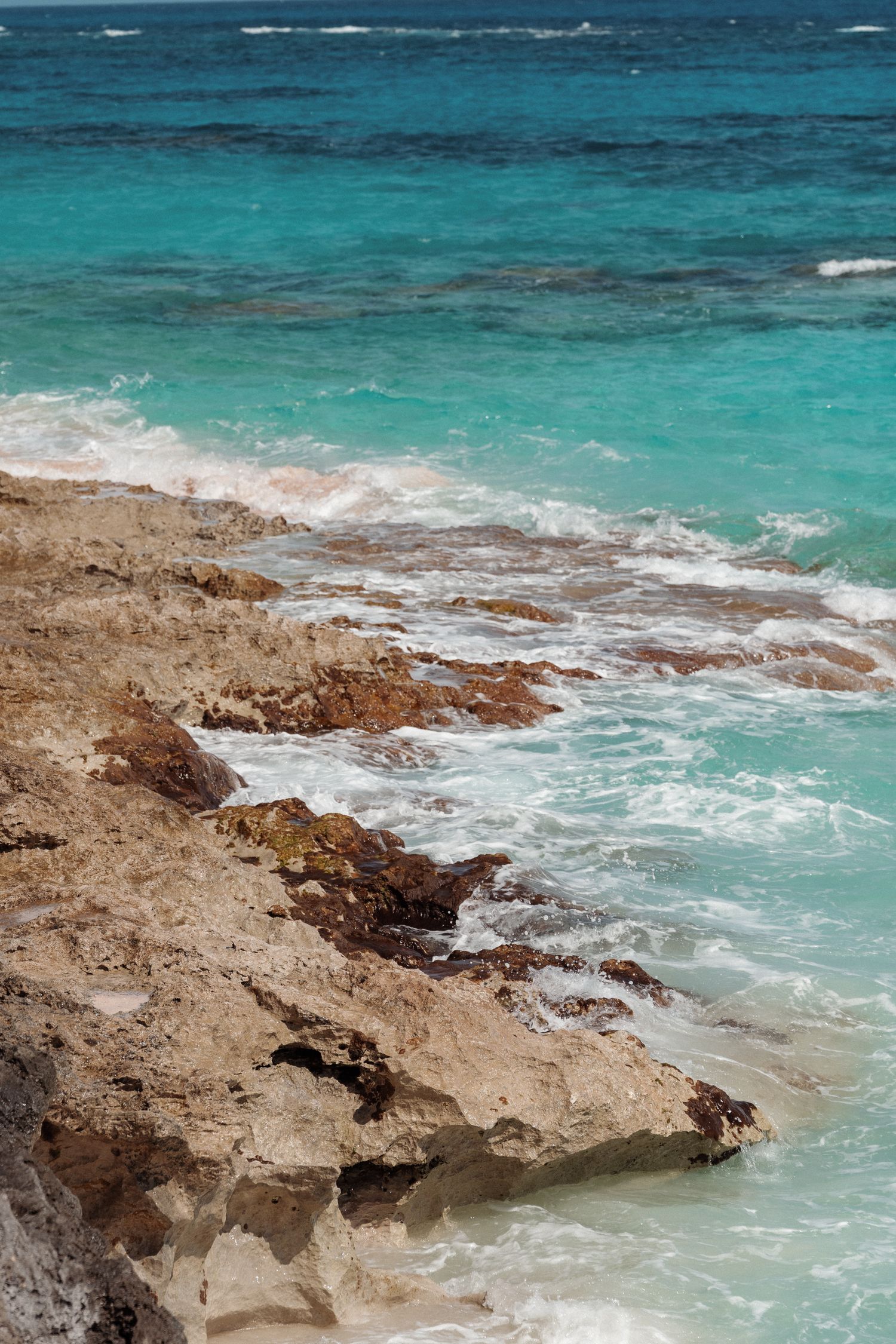 A scenic view of a rocky coastline with clear turquoise water and waves crashing against the shore.