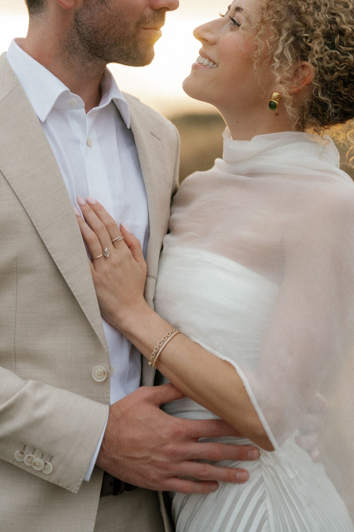 Romantic close-up of couple in wedding attire embracing against neutral background.