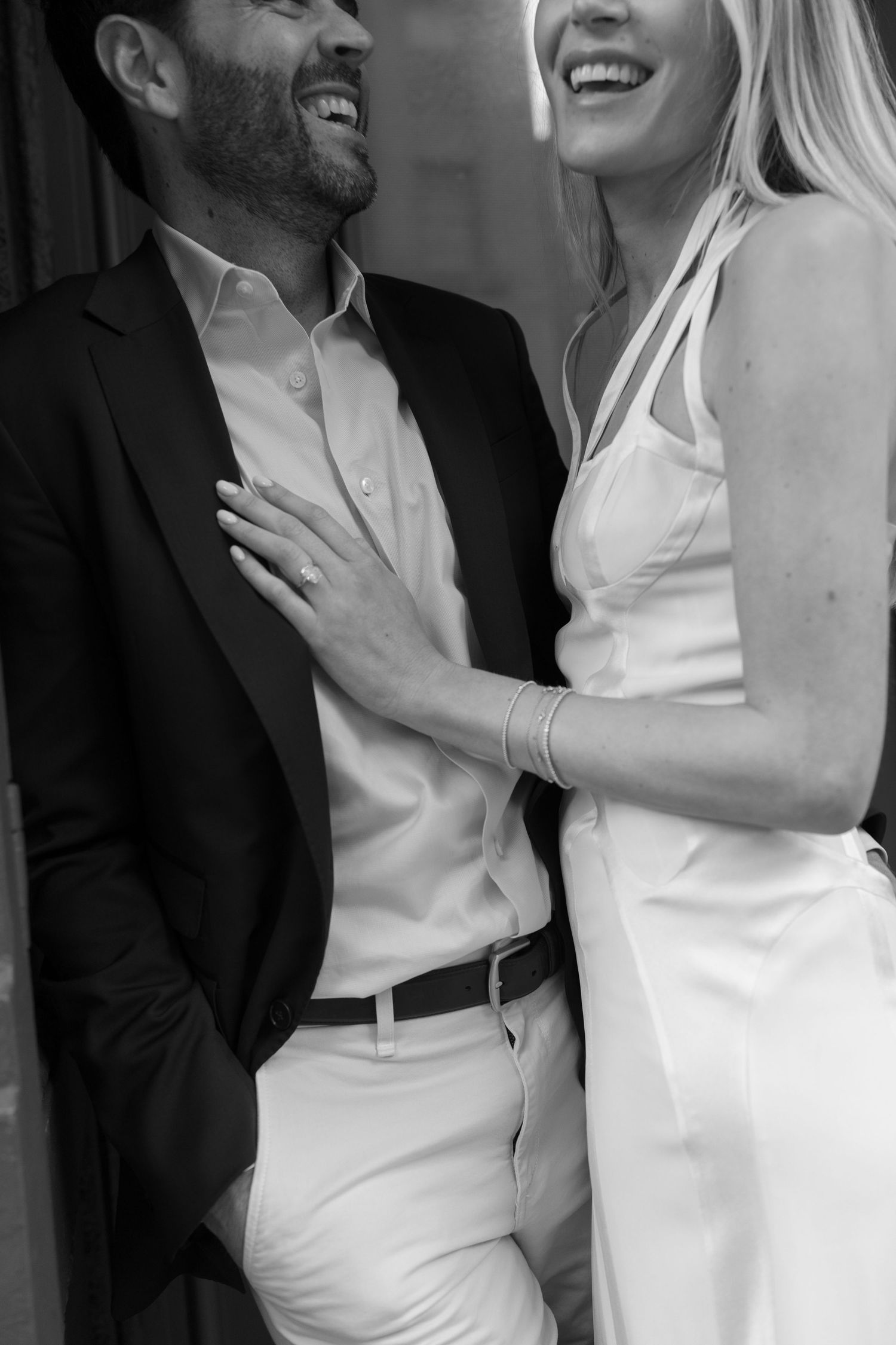 A couple in formal black and white attire embrace and laugh together.