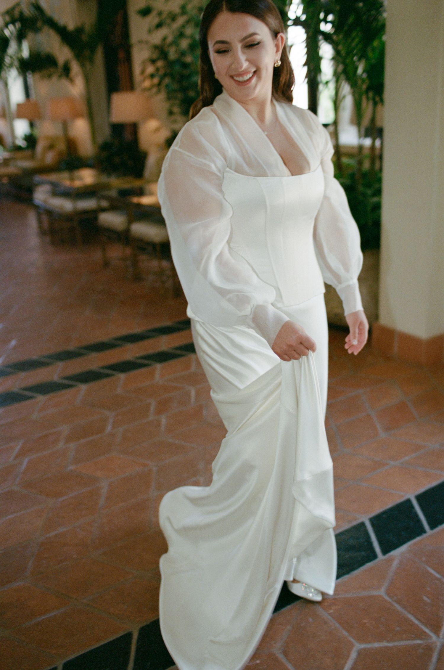 A bride walks gracefully in a modern white wedding gown with statement sleeves on terracotta flooring.