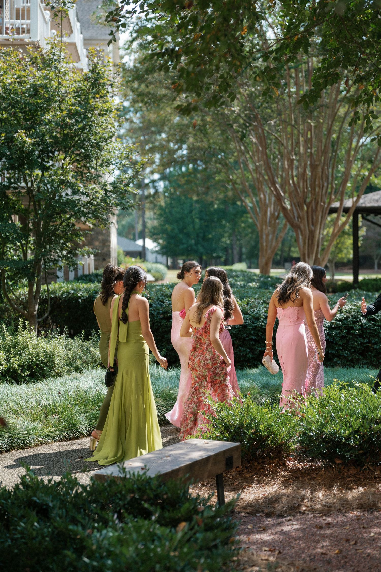 Bridesmaids in pink and chartreuse dresses walk through a garden setting during a wedding photo session.